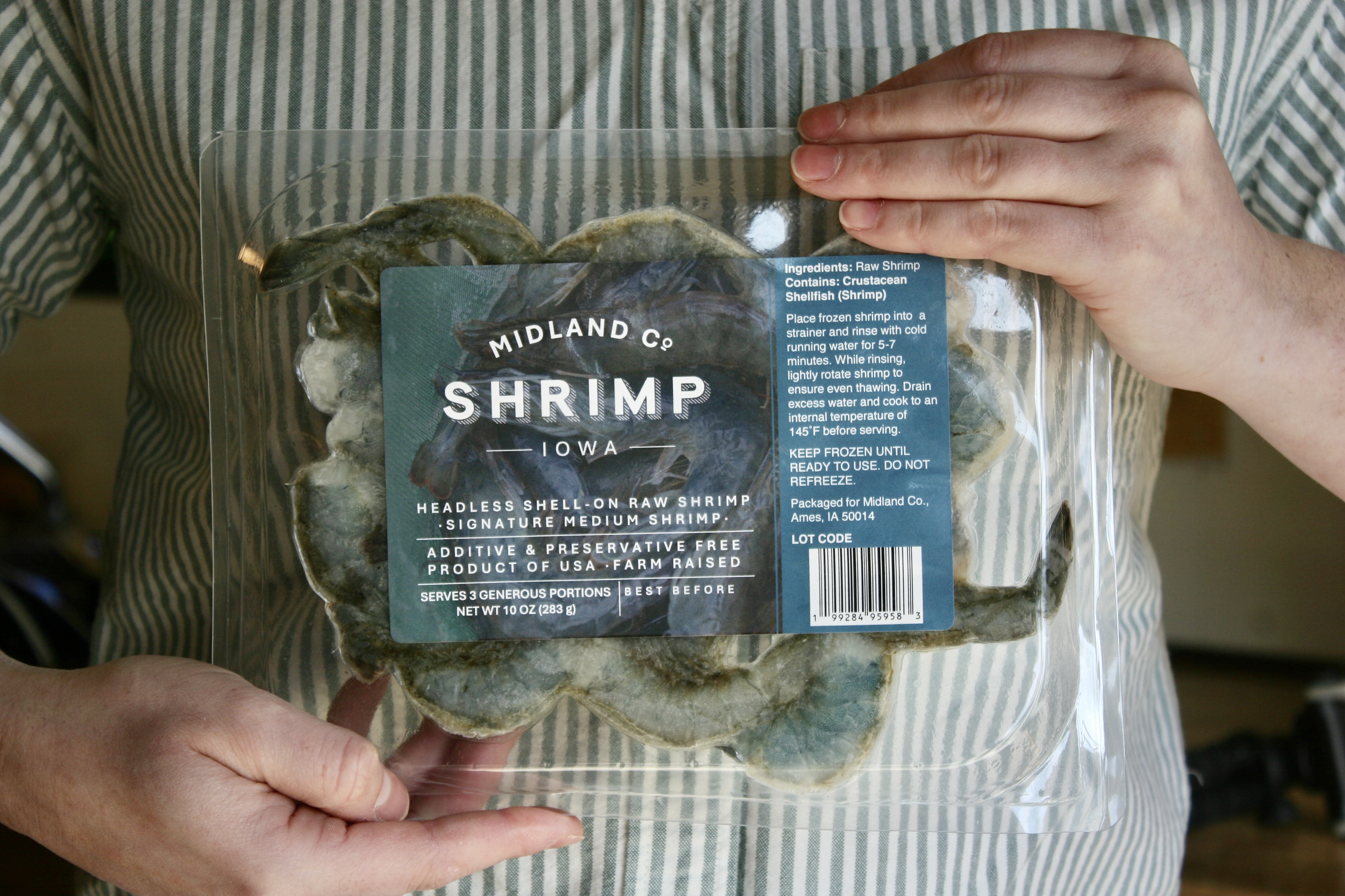 Hands holding a package of Midland Co. Iowa-raised shell-on raw shrimp